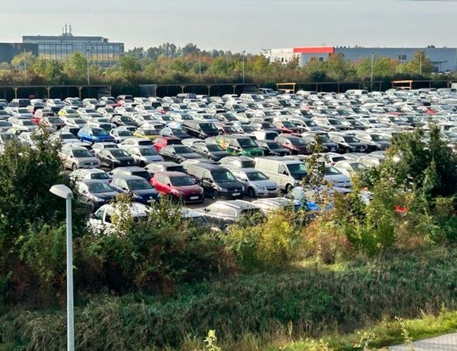Parkeringsplass P365 - Stor bilparkering. Område omgitt av grøntområder. I bakgrunnen er bygninger synlige.