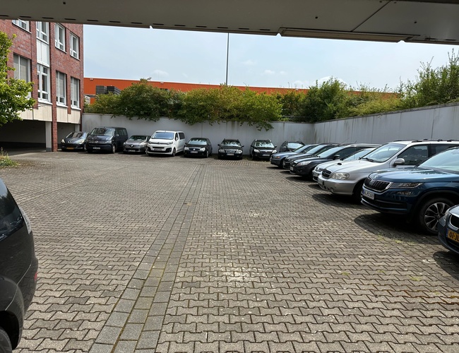 Parking Marspark Outdoor Valet – auta stoją na zewnętrznym placu. Teren jest brukowany i otoczony murem. Po lewej stronie widać budynek.
