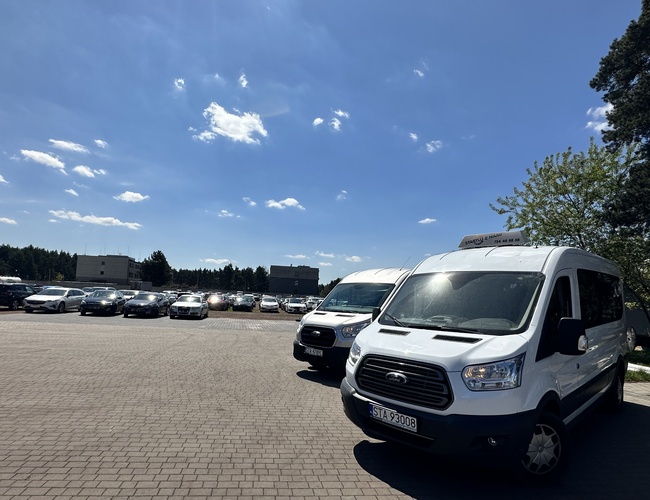 Empieza con nosotros – Hay coches estacionados en el aparcamiento. Algunos de ellos son furgonetas blancas. En el extremo se puede ver el verde.
