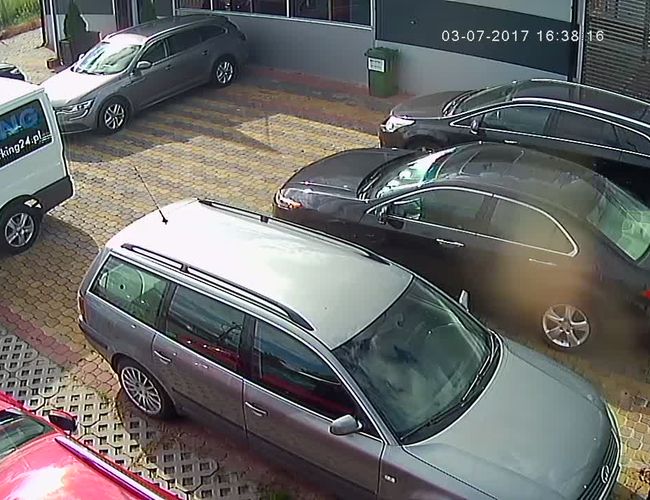 PARKING P24 PREMIUM – Kilka aut stoi na wyłożonym kostką placu. Teren jest ogrodzony i przy budynku.