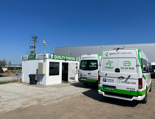 Q-Parking – Kontajner na úrad a dve biele dodávky. Pozemok je štrkový a neobohnaný.