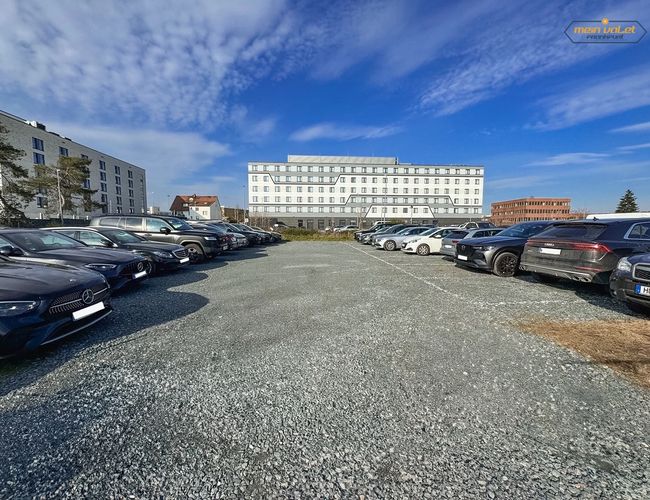 Parking Mein Valet Outdoor – Na żwirowym placu stoją zaparkowane auta. W tle widać kilka budynków.
