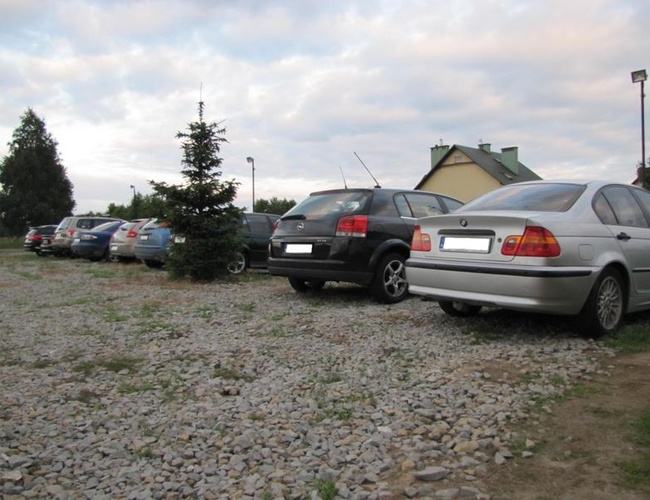 Parkovisko Auto Park – autá stoja na štrkovom povrchu. Vedľa sú stromy a osvetlenie. V pozadí je vidieť budovu.