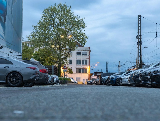 Parkplatz Reinigungs-Valet-Parkservice – Reihe geparkter Autos entlang der Straße. Im Hintergrund Gebäude und Laternen. Ein Baum steht daneben.