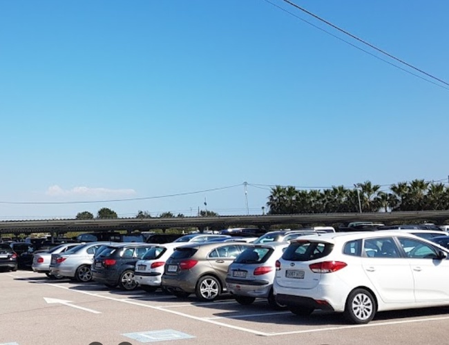 Victoria Parking Alicante – Los coches están aparcados en un espacio abierto. Palmas y cielo visibles.