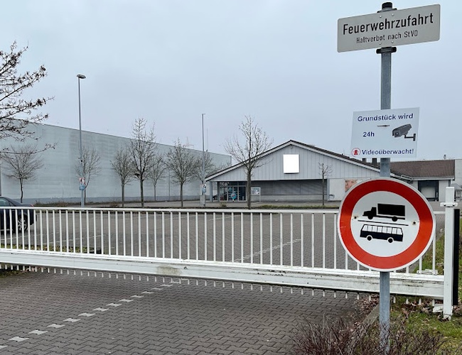 Parkovanie Mein-letiskoparkovisko-Frankfurt P2 - Oplotený priestor s vjazdovou bránou. Značka upozorňuje na zákaz vjazdu nákladných vozidiel a autobusov. Priestor je monitorovaný nonstop.