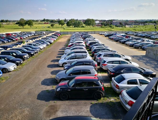 Parking Darex - Na zdjęciu widać parking z wieloma autami. Teren jest dobrze zagospodarowany i ogrodzony. W tle rośnie kilka drzew.