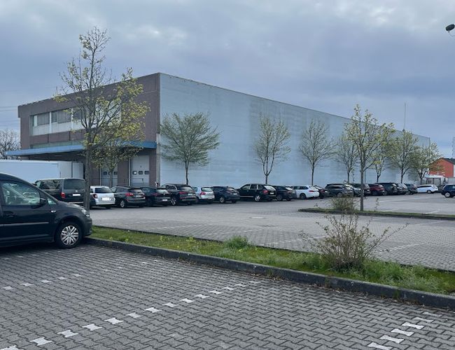 Parkering Mein-Flughafenparkplatz-Frankfurt P2 – Biler står i rekker ved bygningen. Området er belagt med belegningsstein og delvis skogkledd.