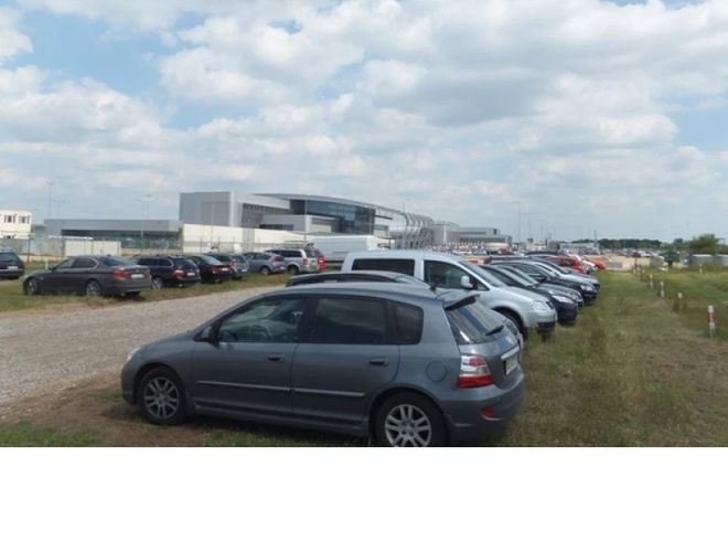 VALET Parking – Rząd zaparkowanych samochodów na trawiastej powierzchni. W tle duży budynek. Teren jest nieogrodzony.