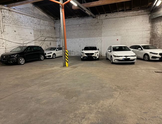 Parking Park Elite Valet - Kilka samochodów zaparkowanych w przestronnej hali. Wnętrze jest murowane i dobrze oświetlone.