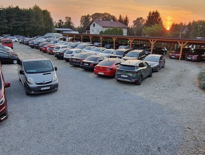 Parking PARK4YOU - Na parkingu stoją samochody osobowe i dostawcze. Teren jest utwardzony i dobrze widoczny. Z tyłu widać zadaszenie.