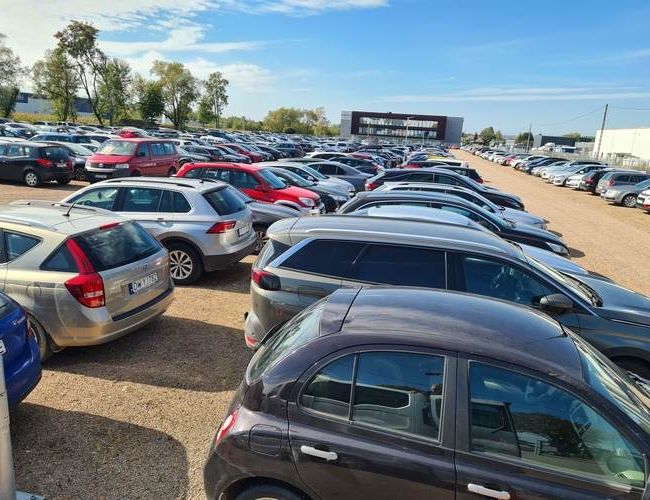 Smart Premium Parking – parking na otwartym terenie. Wypełniony samochodami. W tle widoczny jest budynek.