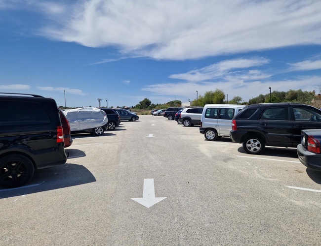 Monster Parking – Veľké, otvorené parkovisko s autami na oboch stranách. Na oblohe sú biele obláčky a modrá obloha.