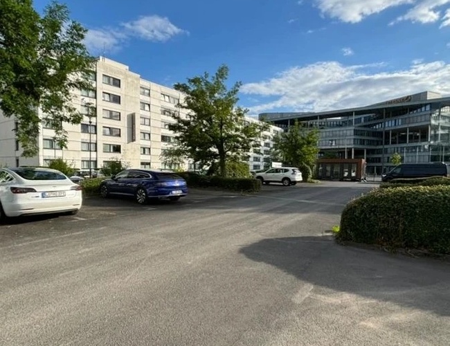 Najvyšší parkovací sluha - Na parkovisku stoja zaparkované autá. V pozadí sú viditeľné budovy a zelené stromy. Pozemok je otvorený a priestranný.