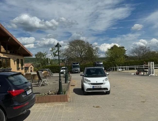 Parking ParkNow Frankfurt - Na parkingu stoją samochody. W tle widoczna jest zieleń i budynki. Teren jest przestronny i otwarty.