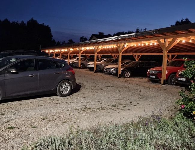 Aparcamiento PARK4YOU - Foto nocturna del aparcamiento cubierto. Los coches están bajo un toldo de madera. La suave iluminación crea un ambiente agradable.