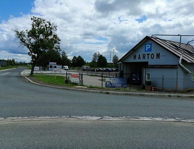 Aparcamiento MARTOM - En la foto se puede ver un área de estacionamiento cercada. Hay un edificio con un letrero y varios coches.
