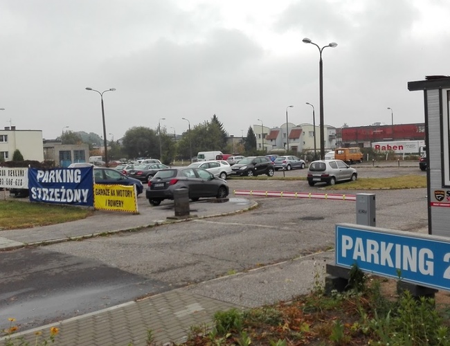 Parkovisko JM Auto - Miesto zaparkovaných áut. Viditeľná strážnicová stánka a tabuľka "Parkovanie 24h".