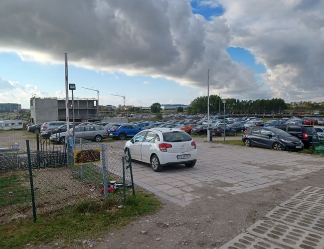 Parking Goliat - Plac jest ogrodzony i nieutwardzony. Na terenie stoją samochody osobowe.