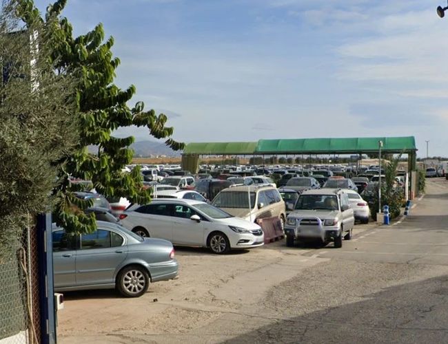 Parking Drimo Park Valet - Na placu stoją liczne samochody. Część miejsc jest zadaszona zielonymi markizami. W tle widoczne jest ogrodzenie.