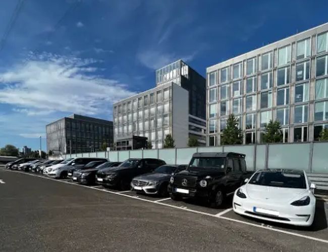 Parking Park2Travel Valet Outdoor - Samochody stoją w rzędzie na otwartym parkingu. Tło stanowią nowoczesne biurowce i błękitne niebo.