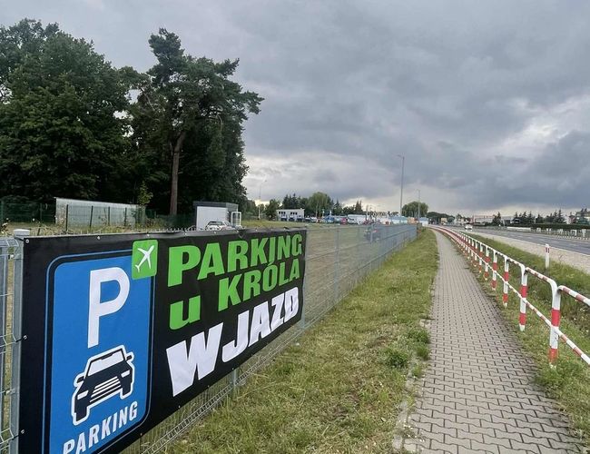 Baner parkingowy na ogrodzeniu "Parking u Króla" z wskazaniem wjazdu na parking