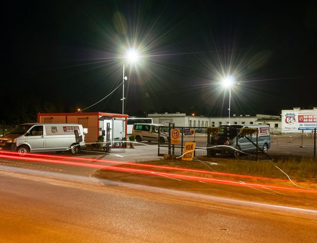 AAP-66 – Nocny parking z dużymi lampami i ogrodzeniem. Widać napis "Wolne miejsca". Teren asfaltowy z zaparkowanymi busami.