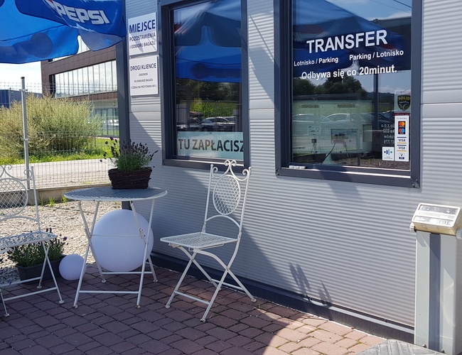 DOBRÉ parkovanie - Pri vstupe je stôl a stoličky. Vedľa sa nachádza informačná tabuľa a reklama na transfer.