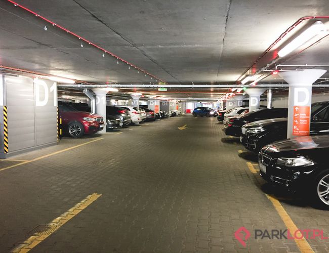 Oficjalny Parking Lotniska P2 - Podziemny parking z zaparkowanymi samochodami. Oświetlony, oznaczone sekcje.