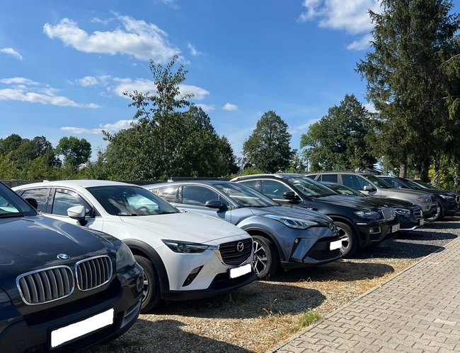Parking Beta - Gobierno de coches aparcados sobre un terreno de grava. Al lado hay una acera de adoquines. En el fondo se ven árboles.