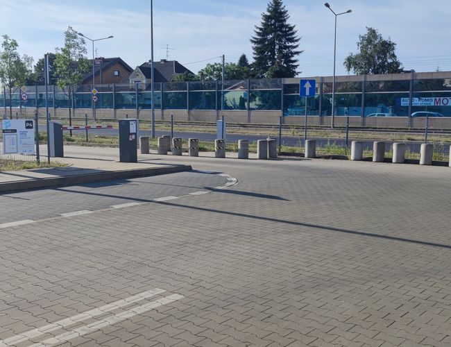 Офіційна паркінг P4 - в'їзд з опущеним шлагбаумом. Паркінг огороджено сіткою. Видно вертикальні знаки та бетонні стовпчики.