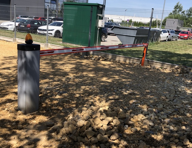 Parkovisko počas sviatkov – Závorka blokuje vjazd. Areál je oplotený. Na pozadí je vidieť budovu a zaparkované autá.