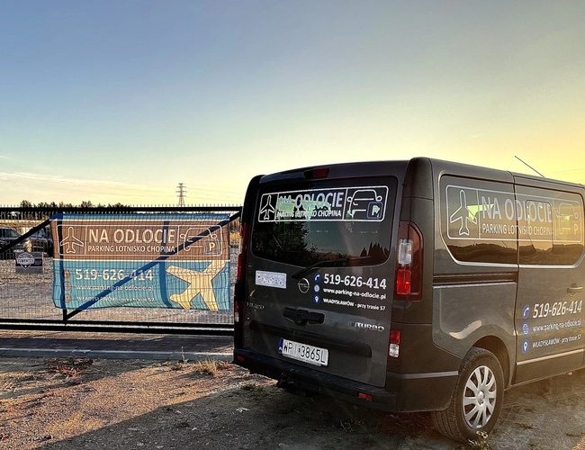 Parkovanie Na Odlete – Pozemok je ohradený kovovou sieťou. Pred bránou stojí označený autobus.