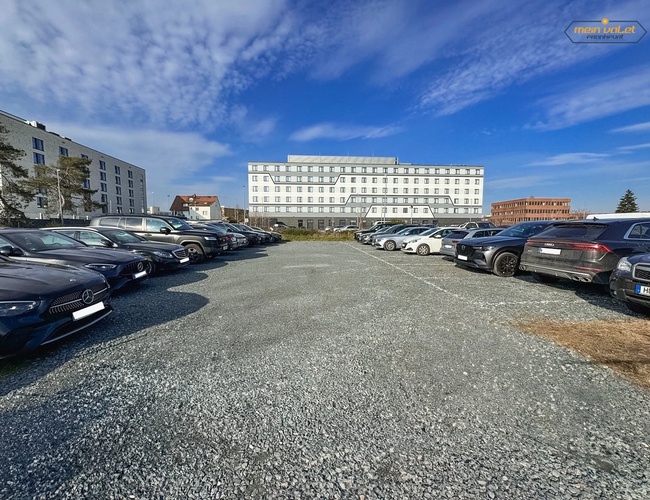 Parkovanie Moje Valet Outdoor – Na štrkovom námestí stoja zaparkované autá. Na pozadí je vidieť niekoľko budov.