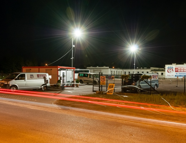 AAP-66 – Nocny parking z dużymi lampami i ogrodzeniem. Widać napis "Wolne miejsca". Teren asfaltowy z zaparkowanymi busami.