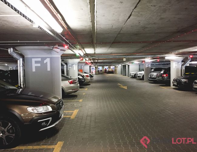 Oficjalny Parking Lotniska P2 – podziemny parking z autami. Kolumny oznaczone F1. Miejsca jasno oświetlone.