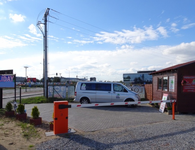 Parkovanie na sviatky Gdaňsk - Parkovisko s bránou a budovou kancelárie. Na dvore je zaparkované svetlé autobus. Pozemok je ohraničený a udržiavaný.