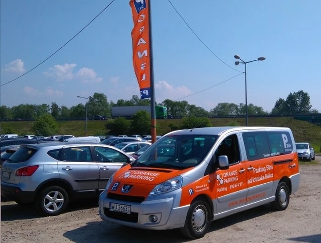 Orange Parking P3 – Na parkingu stoi pomarańczowy bus reklamowy. Obok niego zaparkowane są inne samochody. W tle powiewa flaga z napisem.