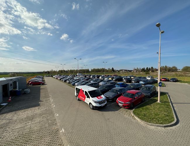 Entdecken Sie das GDN-Parkhaus – ein großzügiger Platz mit vielen Autos. Das Gelände ist befestigt und beleuchtet. Nebenan steht ein weißes Fahrzeug.