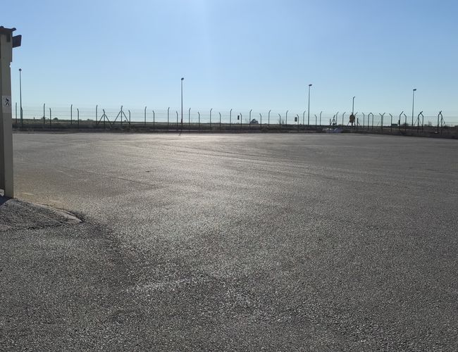 Parking Odkryj-Auto - Duży, ogrodzony plac z latarniami. Po lewej zadaszone stanowisko. Na horyzoncie widoczny płot.