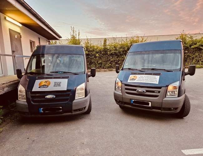 Sun Park Airport Parking Outdoor – Dwa niebieskie samochody stoją na placu. Przy ścianie budynku widać oświetlenie. W tle rosną krzewy.