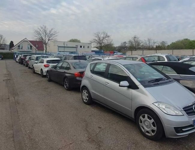 Parking Weltparking – na parkingu stoją zaparkowane samochody. Teren jest ogrodzony. W tle widoczny jest budynek.