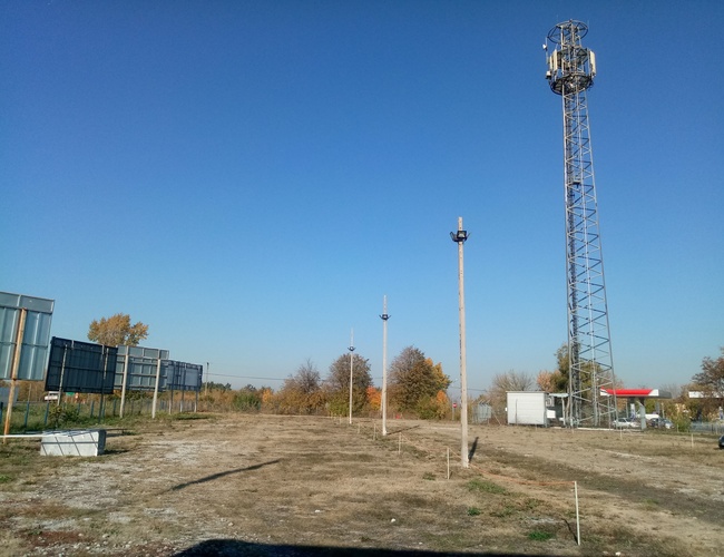 Parking Bastion – plaza con césped y mástiles. En el fondo se ve una torre de telecomunicaciones. El área no está cercada.