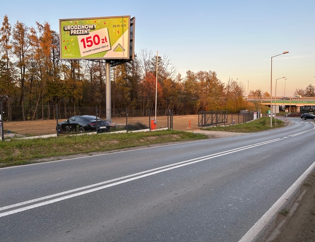 Victory Cars - Estacionamiento vallado con puerta. A lo largo de la carretera hay farolas. Al lado se puede ver un anuncio en la valla publicitaria.