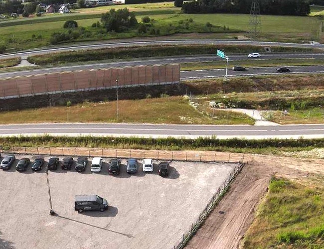 Parkovisko Na Odletu – Na parkovisku stojí niekoľko áut. Oblasť je ohradená. V pozadí je vidieť cestu a polia.