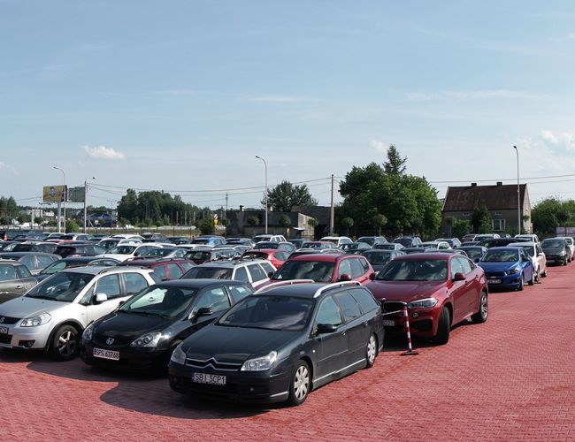 MEGA Parking - Gran plaza abierta con adoquines. Muchos coches estacionados. Al final de la plaza se ve un edificio.