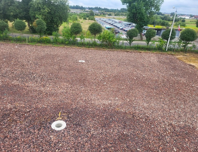 Sky Park - un lugar de grava rodeado de árboles. Al fondo se ve un aparcamiento lleno de coches. Hay varias lámparas de iluminación.