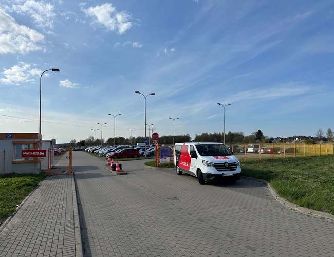 Objav-Parking GDN - Pozemok obklopený plotom. Na parkovisku stoja autá. Vedľa prechádza biely dodávka.