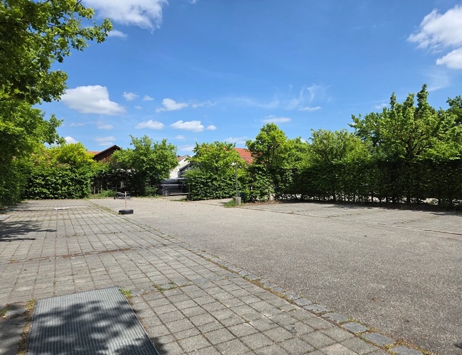 Atomis Hotel Munich Airport Parking – Estacionamiento con plazas disponibles. Está rodeado de arbustos verdes. En el cielo se ven algunas nubes.
