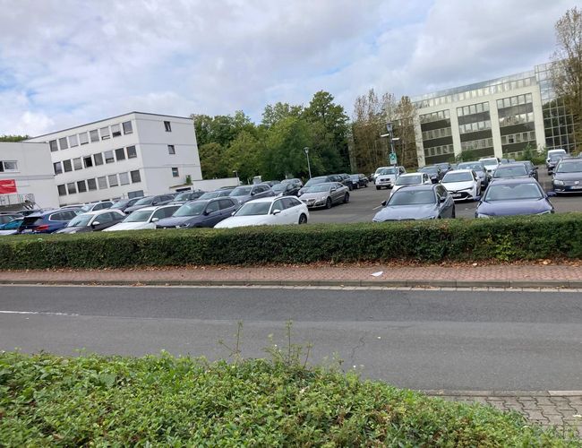 Parking Stern Valet - Na placu stoją zaparkowane samochody. Obok widać budynki biurowe. Teren jest otoczony zielenią.